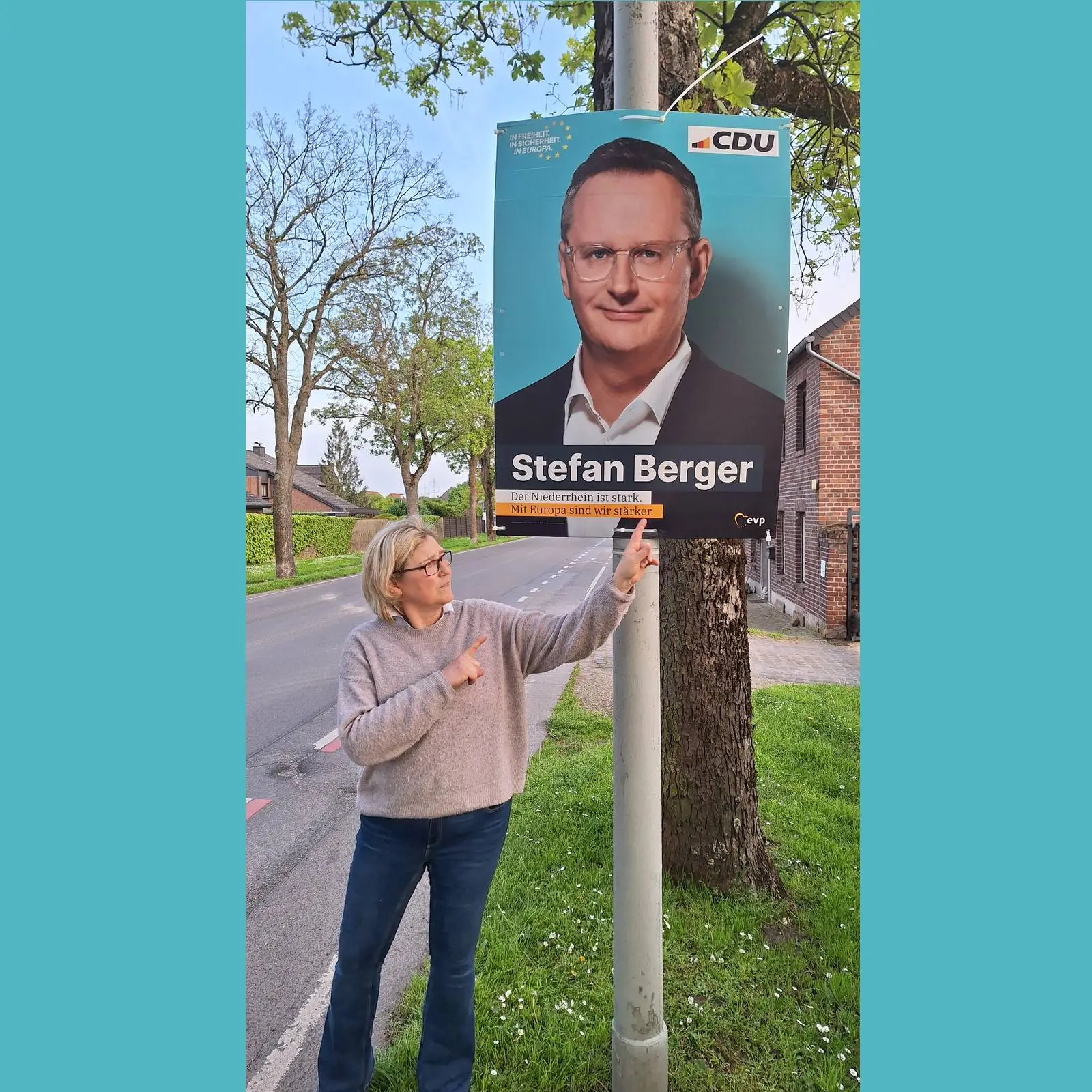Plakat der CDU mit Stefan Berger und Text für die Europawahl am Laternenmast und Nicola Theißen-Fahron,
 die auf das Plakat deutet